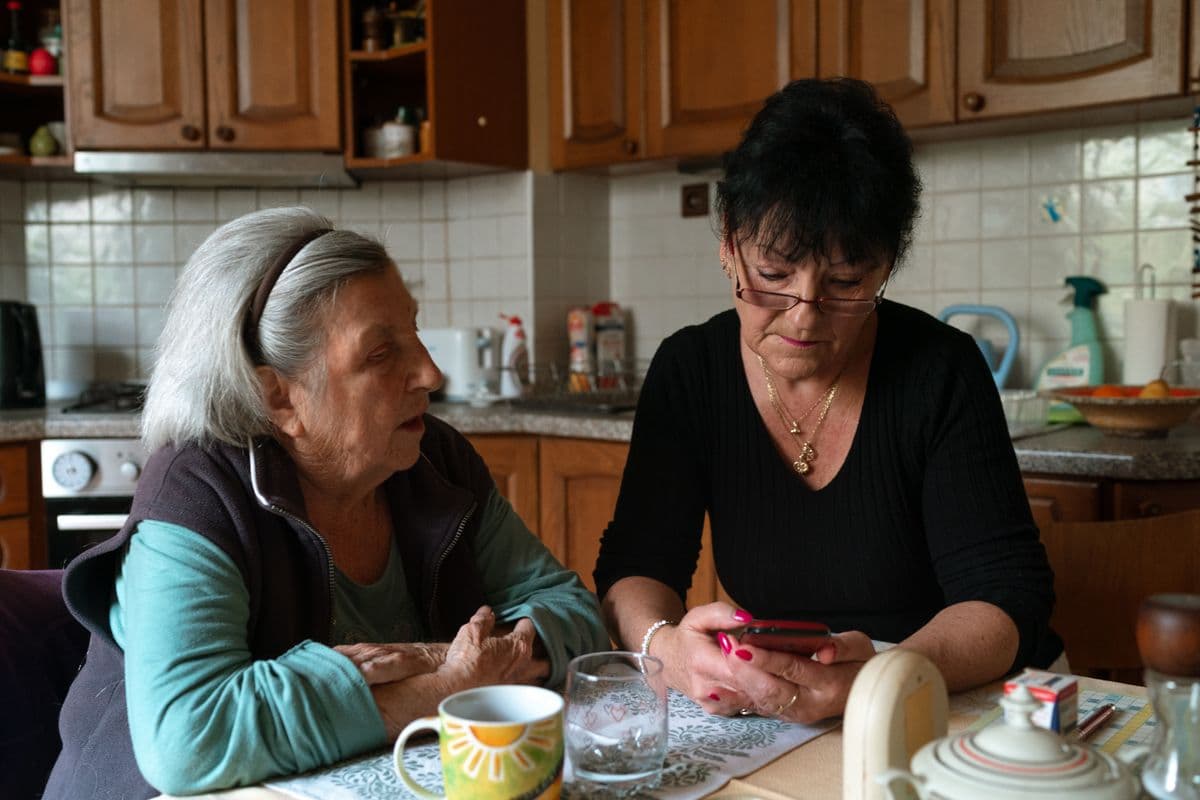 Two women sitting together at a kitchen table, looking at a phone